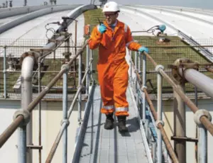 Veolia engineer in orange safety gear walking on a metal walkway inspecting an industrial storage facility.