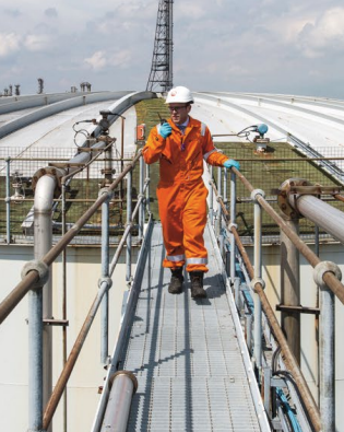 Veolia engineer in orange safety gear walking on a metal walkway inspecting an industrial storage facility.